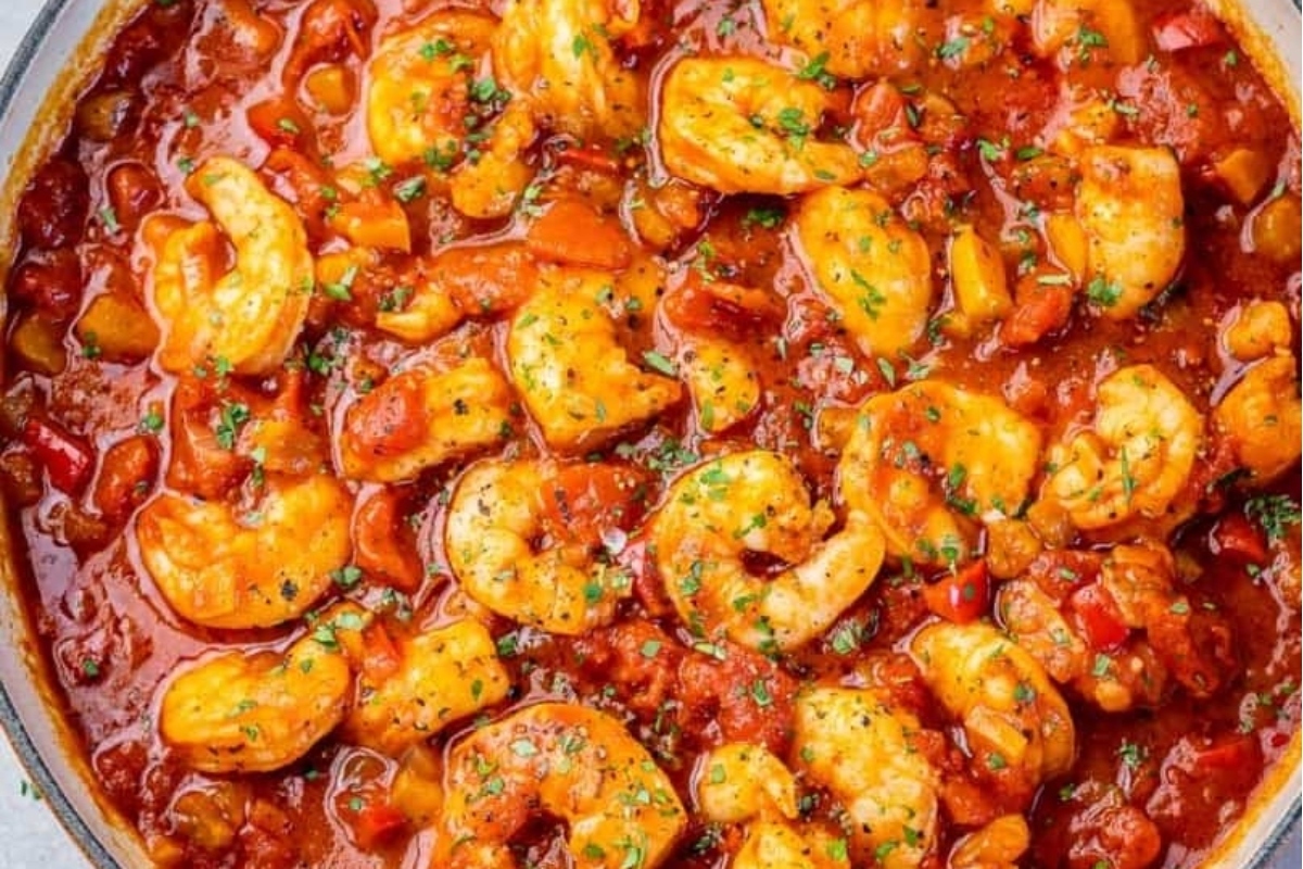 A pan of shrimp cooked in a rich and chunky tomato-based sauce, garnished with herbs.