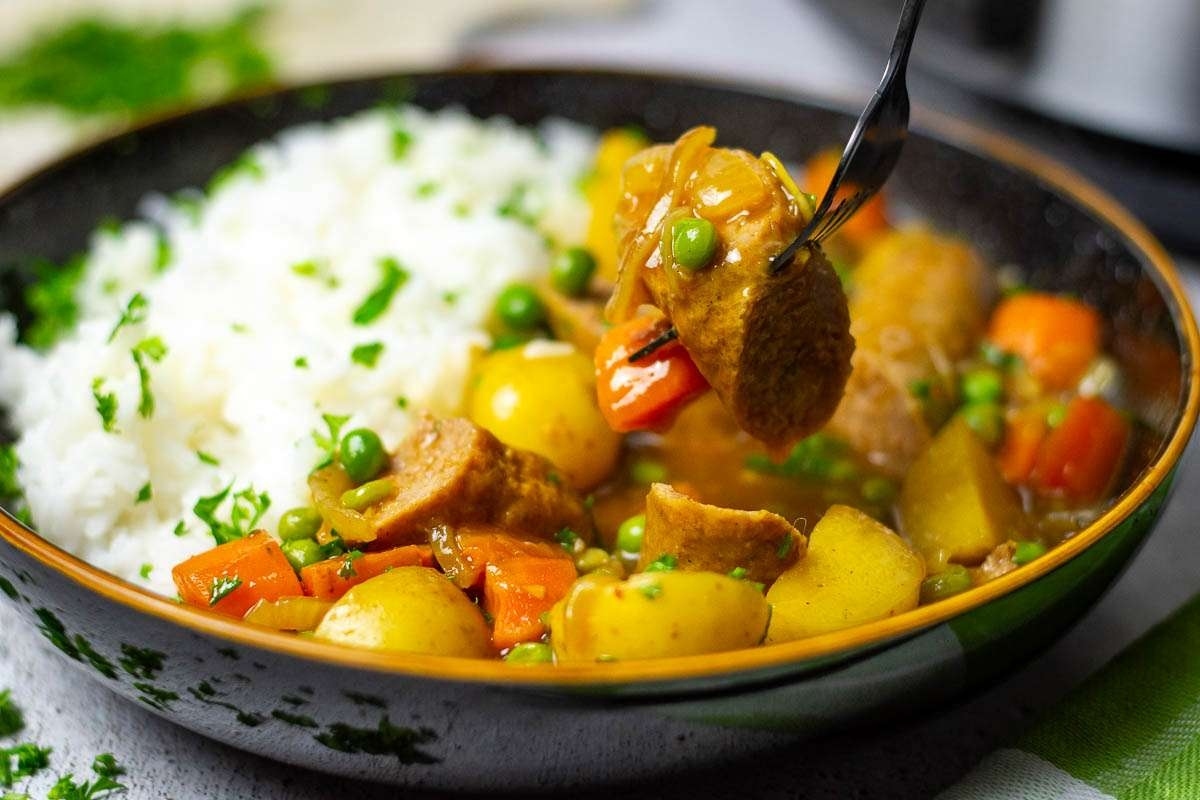 A bowl of curried sausages with a fork.