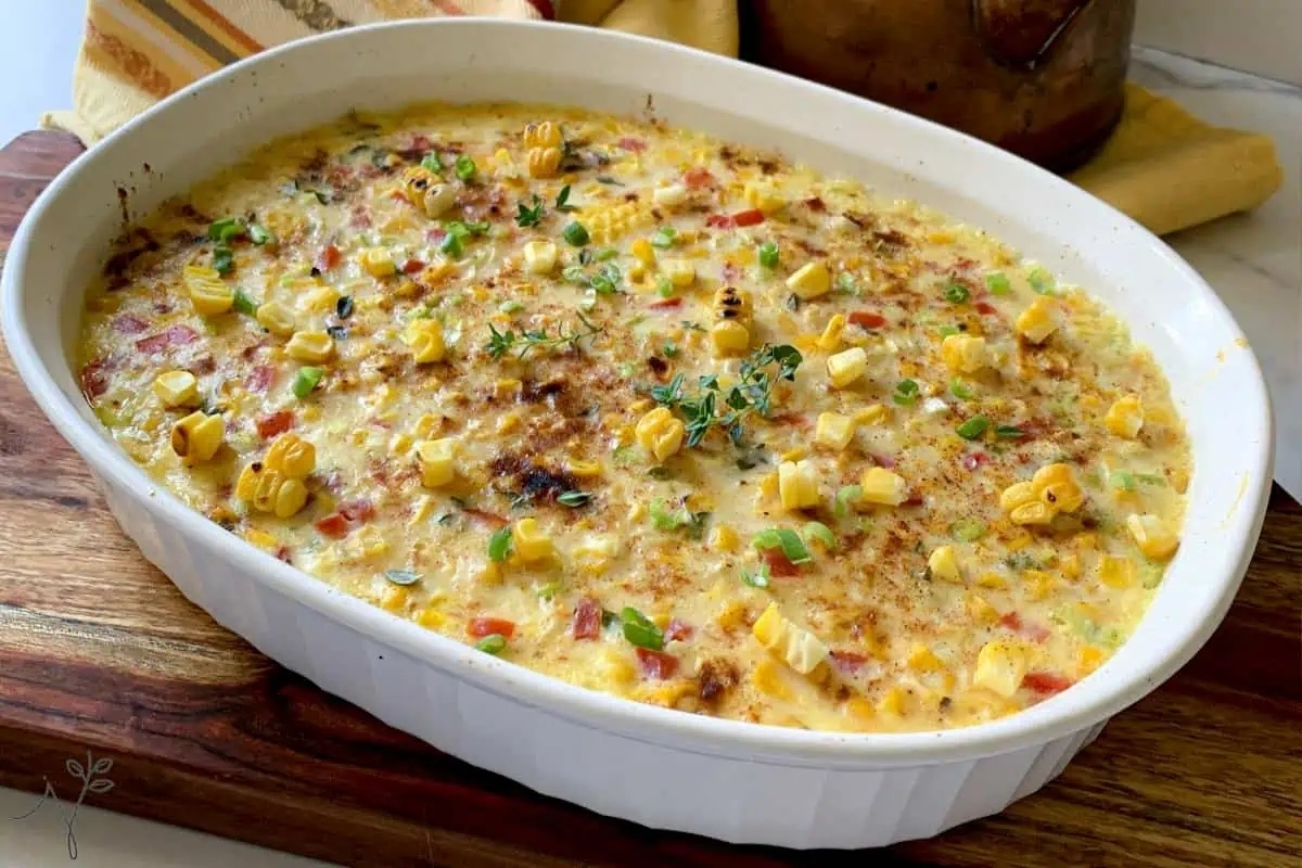 A baked corn casserole with melted cheese and herbs in an oval dish, garnished with fresh thyme.