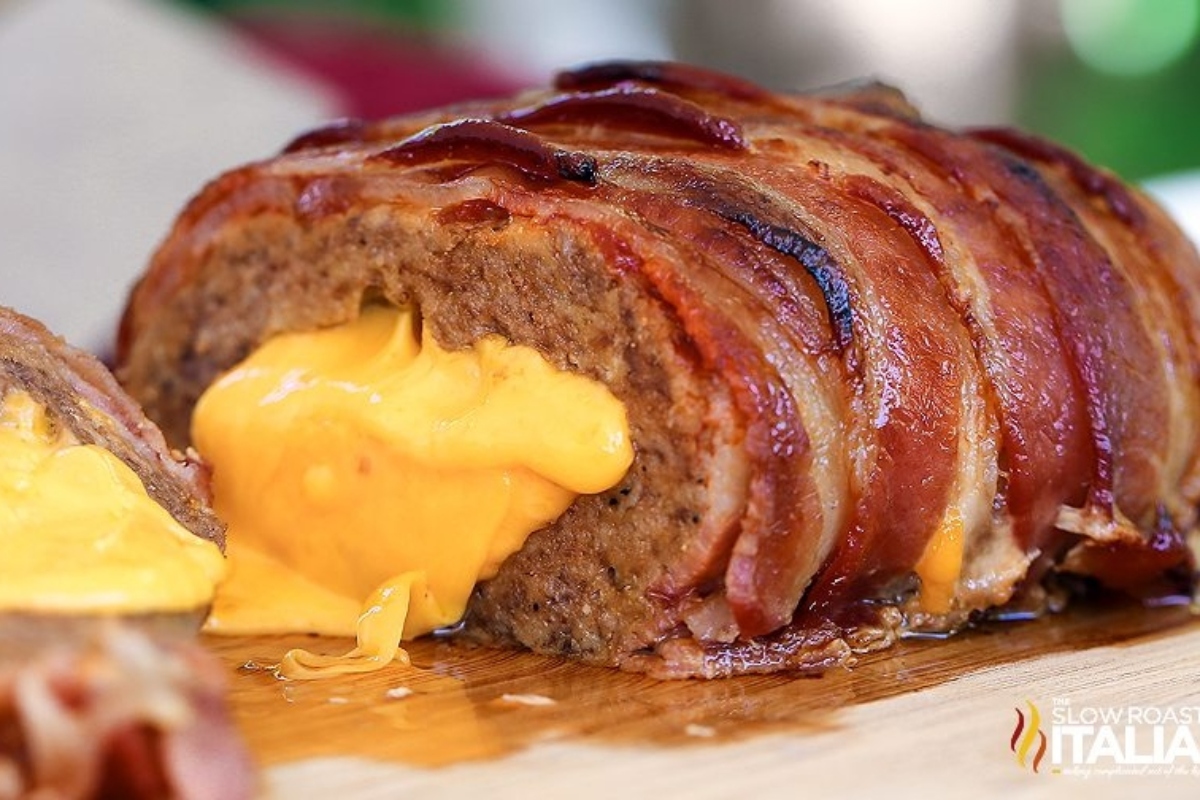 Cheese-stuffed meatloaf wrapped in bacon on a wooden board.