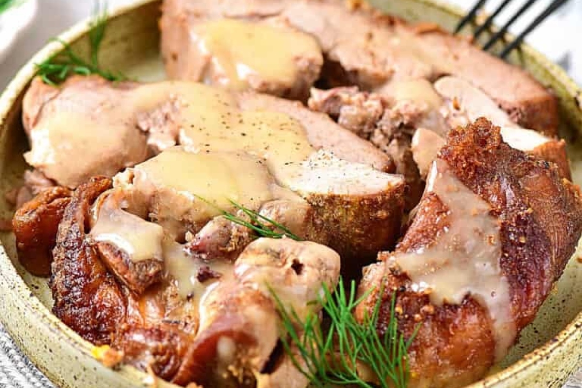 Sliced roasted turkey with gravy and a sprig of dill on a plate.