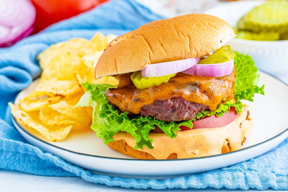 A burger on a plate next to chips and pickles.