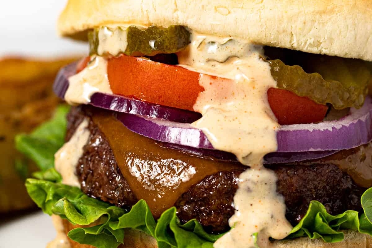 A burger with lettuce, tomatoes, onions and pickles.