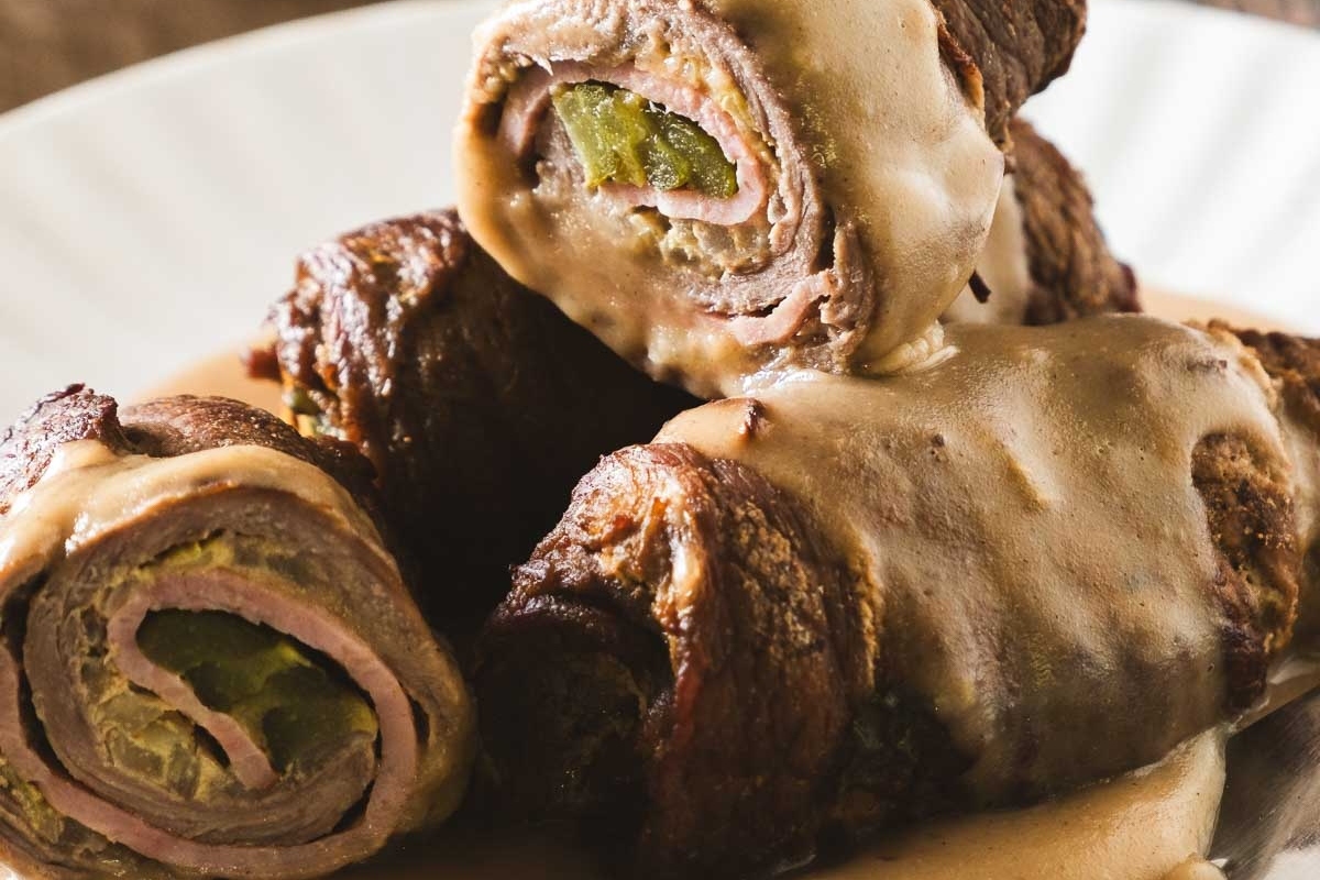 Sliced steak rolls filled with vegetables and topped with gravy on a plate.