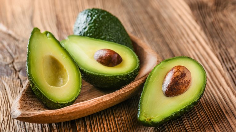 Avocado on old wooden table. Halfs on wooden bowl. Fruits healthy food concept.