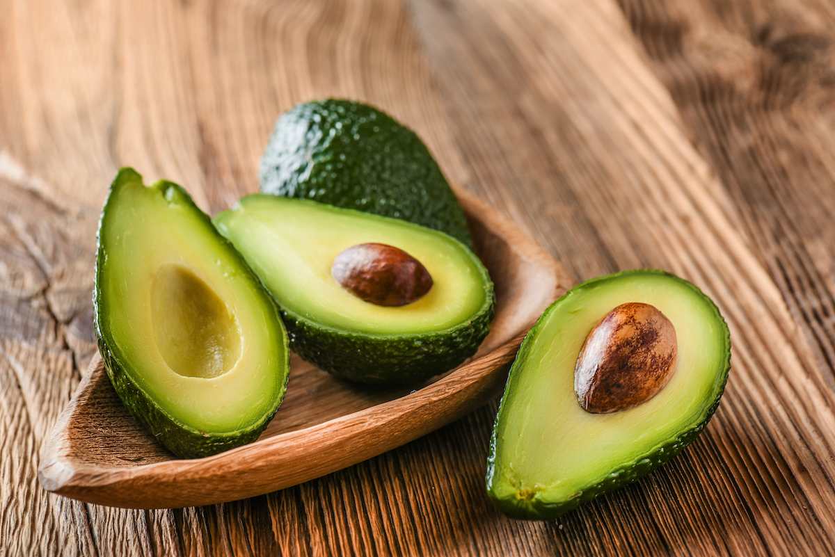 Avocado on old wooden table. Halfs on wooden bowl. Fruits healthy food concept.