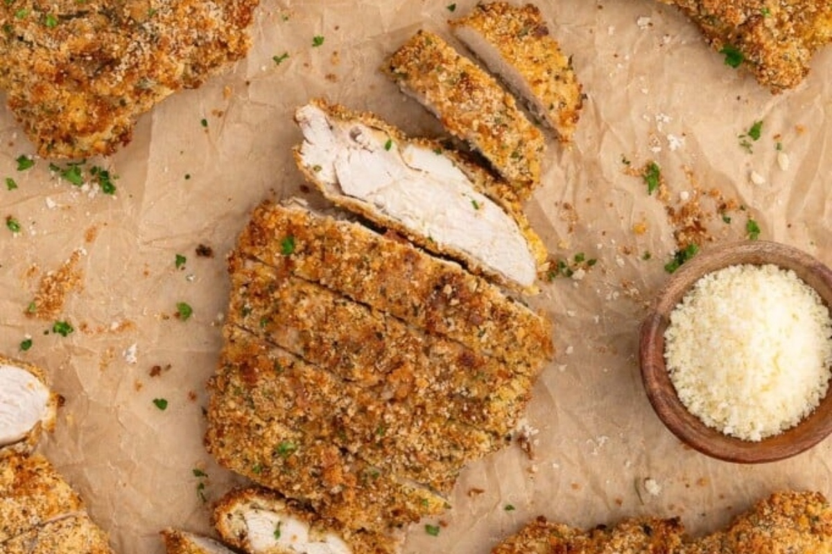 Breaded chicken cutlets served on parchment paper with a side of grated cheese.