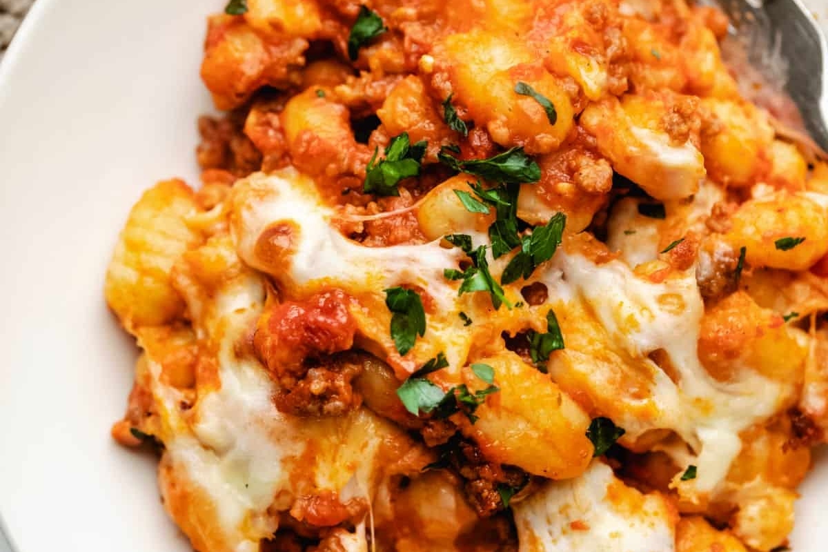 A close-up of a cheesy baked pasta dish garnished with herbs.