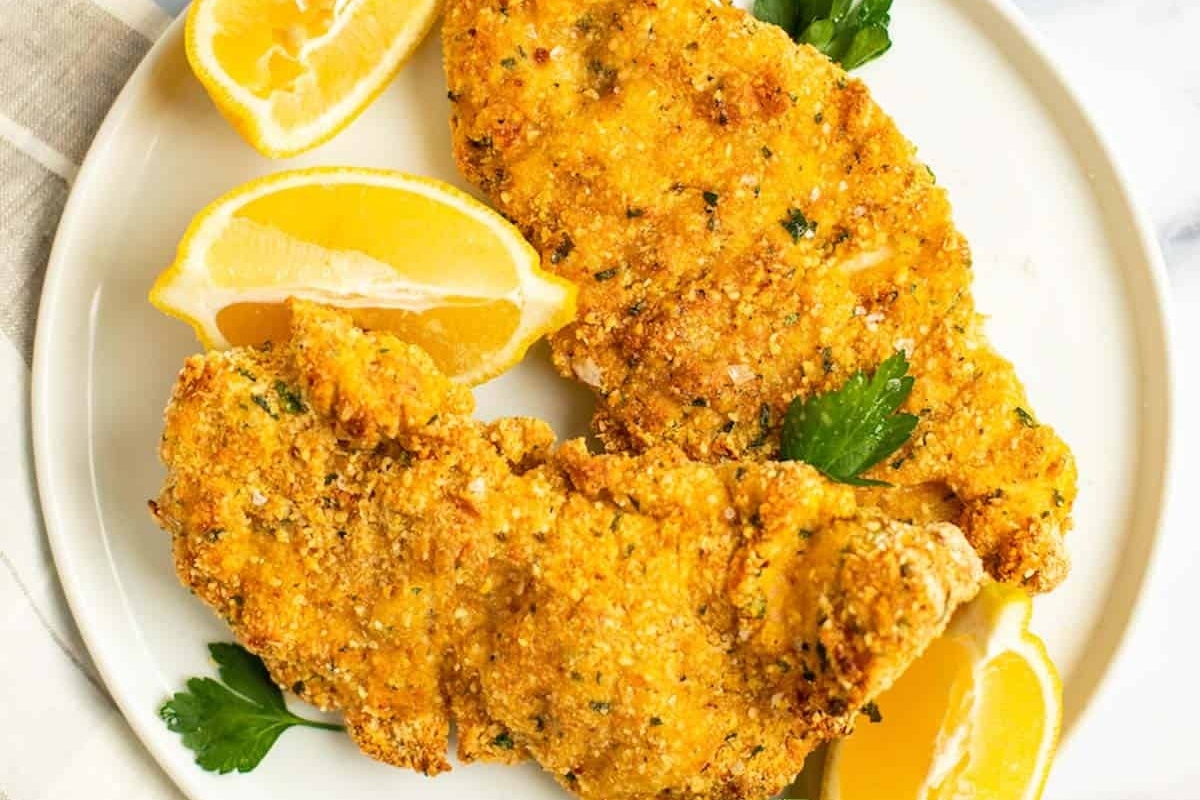 Breaded chicken cutlets with lemon wedges and parsley on a white plate.