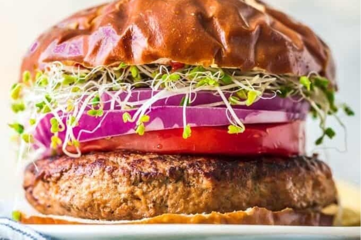 A burger with sprouts and tomatoes on a plate.