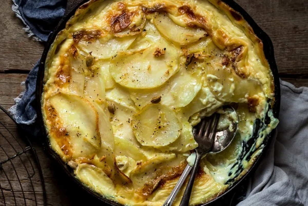 A golden-brown baked potato gratin in a cast-iron skillet, suggesting a freshly cooked, comforting meal.