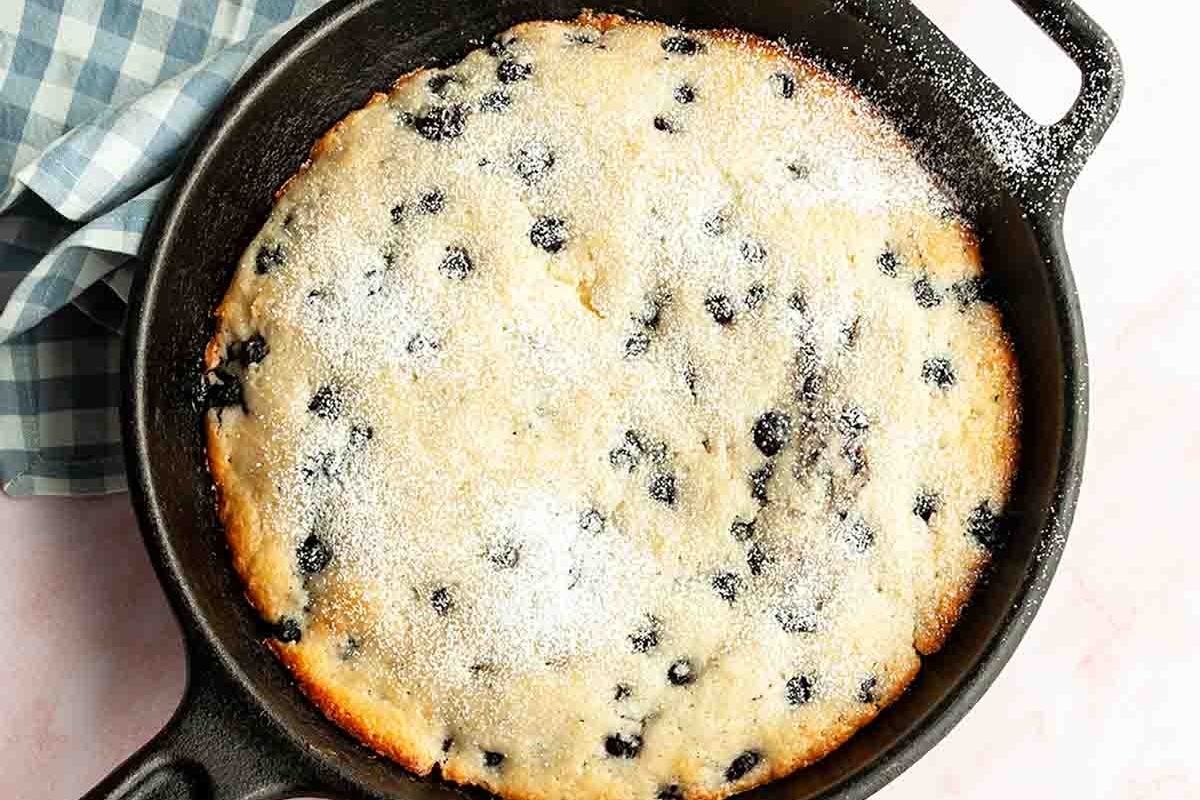 A freshly baked blueberry cobbler in a cast iron skillet, sprinkled with powdered sugar.