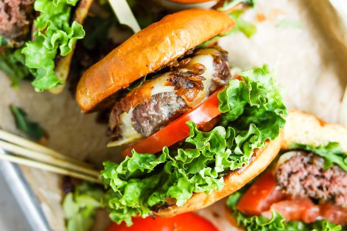 A close-up of a juicy hamburger with lettuce, tomato, cheese, and caramelized onions on a bun.