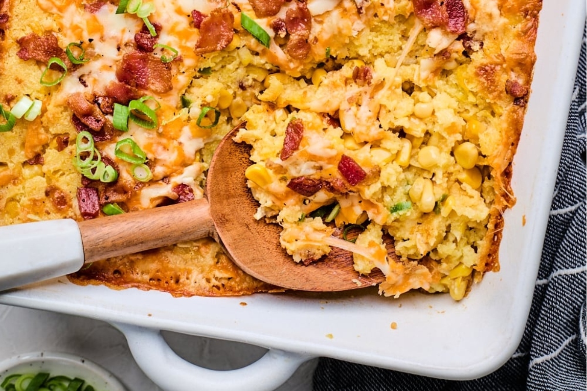 Cheesy corn casserole with bacon and cheese in a white dish.