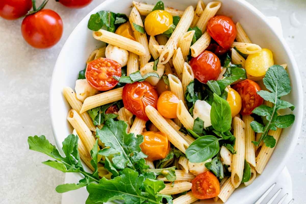 Penne with tomatoes and basil in a white bowl.