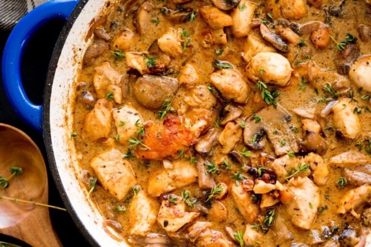 A close-up of creamy chicken and mushroom stew garnished with fresh herbs in a blue pot.
