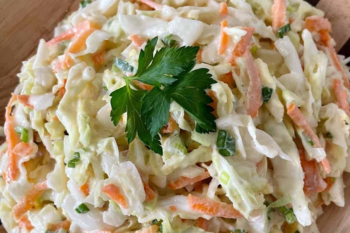 A bowl of creamy coleslaw garnished with a parsley leaf.
