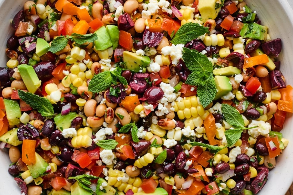 A white bowl with black beans, corn, tomatoes and avocado.