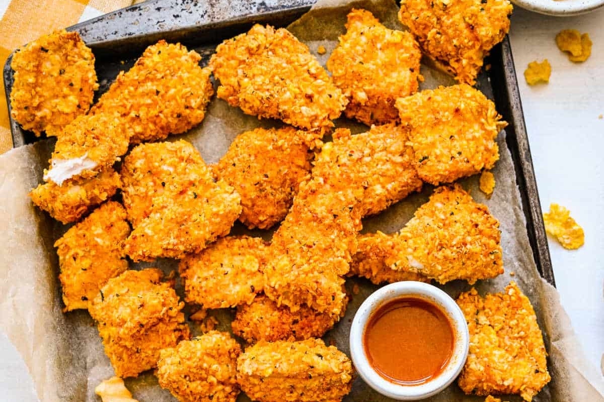 A tray of crispy, golden-brown breaded chicken tenders served with a side of dipping sauce.