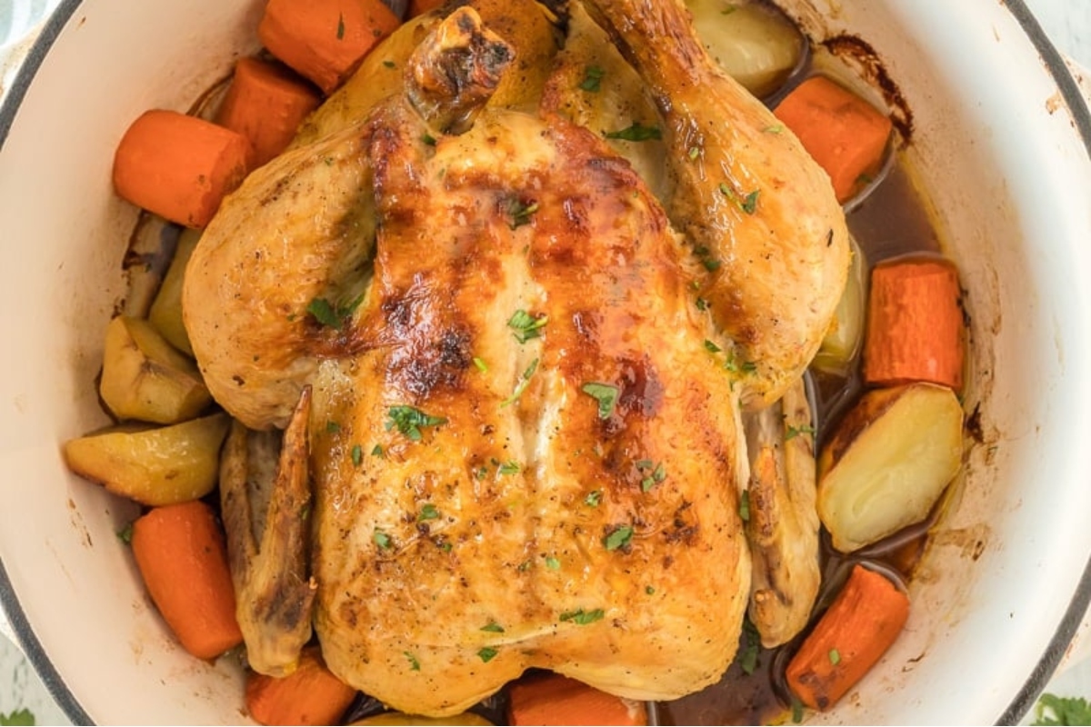 A chicken and vegetables in a white pot.