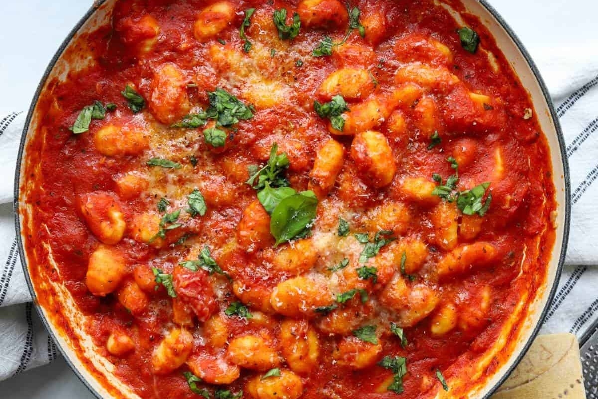 A pan of gnocchi with tomato sauce and sprinkled herbs.