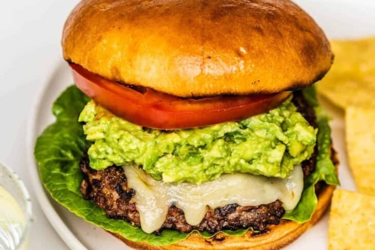 A burger with guacamole and chips on a plate.
