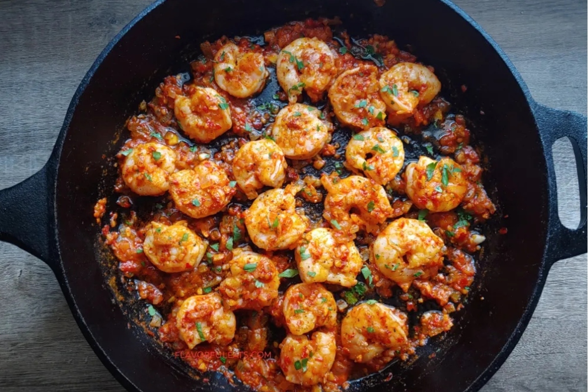 Shrimp cooking in a spicy tomato sauce in a cast iron skillet.
