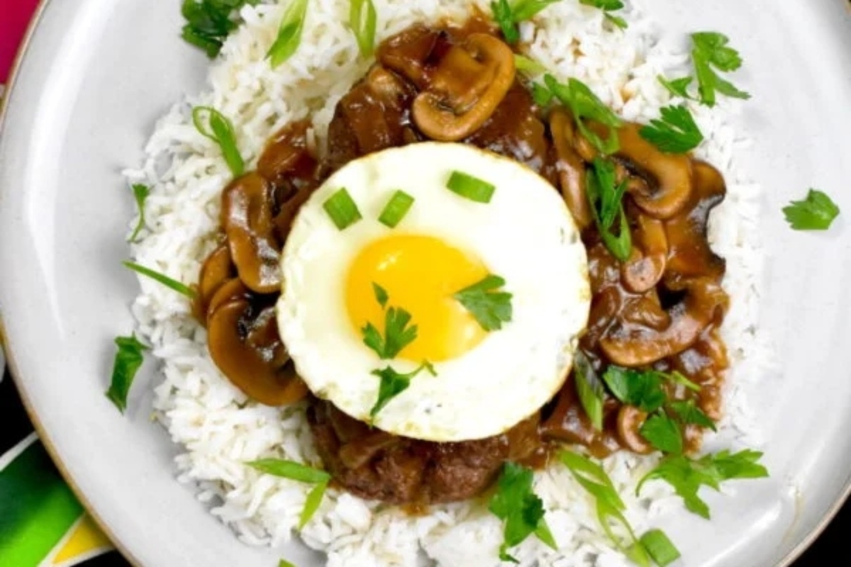 A dish of rice topped with a savory meat sauce, mushrooms, a sunny-side-up egg, and garnished with fresh herbs.