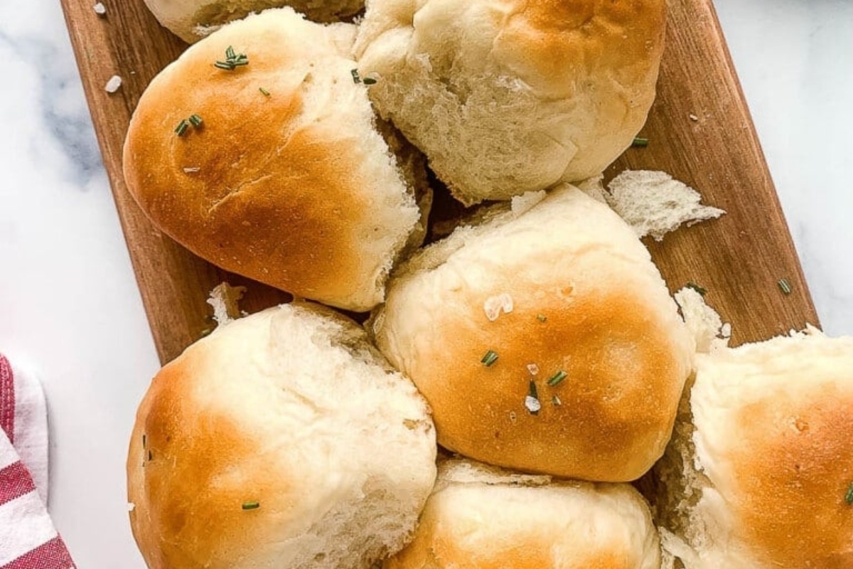 Freshly baked dinner rolls on a wooden board with a sprinkle of herbs on top.