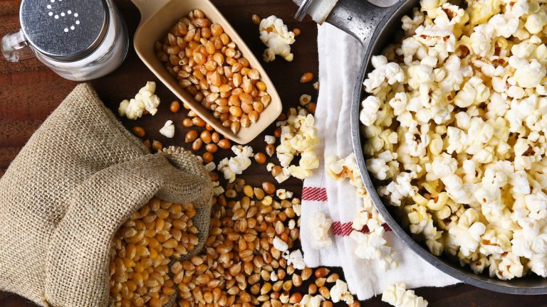 Top view of a pot full of freshly popped popcorn with salt and unpopped kernels on the side.
