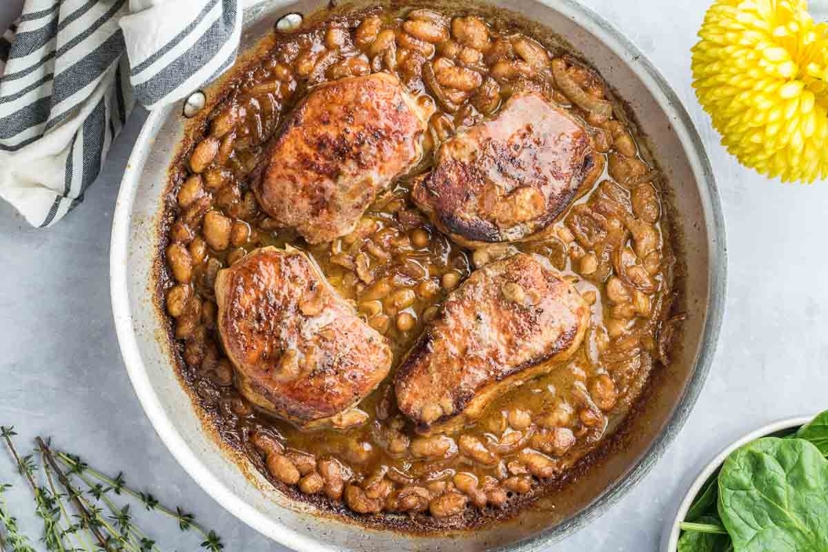 A dish of white beans with seared pork chops in a skillet.