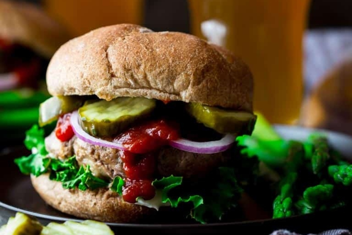 A burger with ketchup and pickles on a plate.