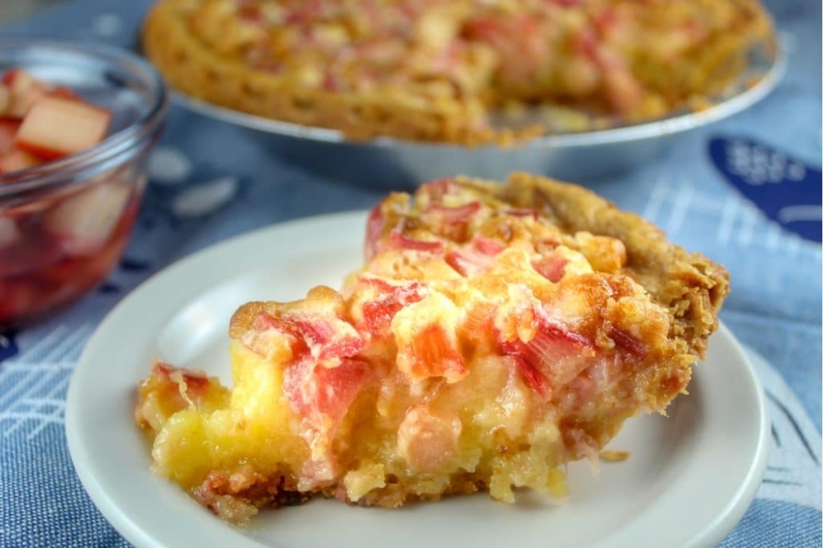 A slice of rhubarb pie on a plate with the whole pie in the background.