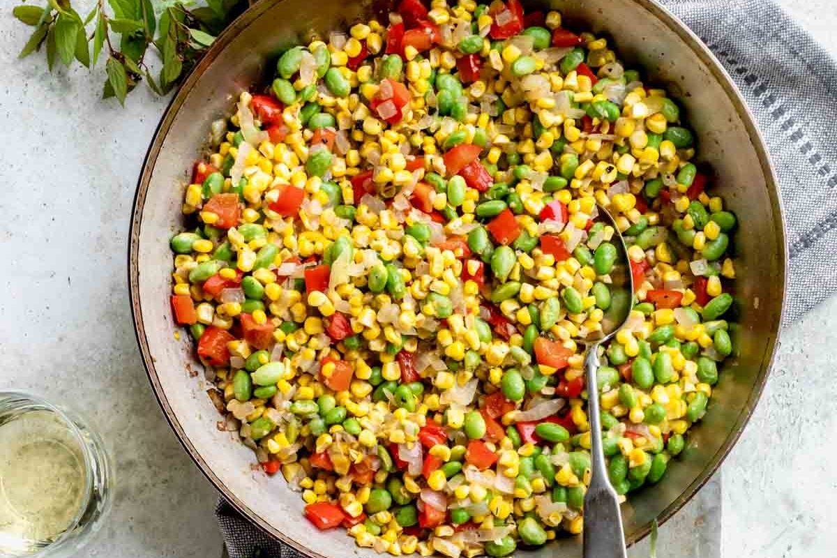 A skillet full of vegetables and corn.
