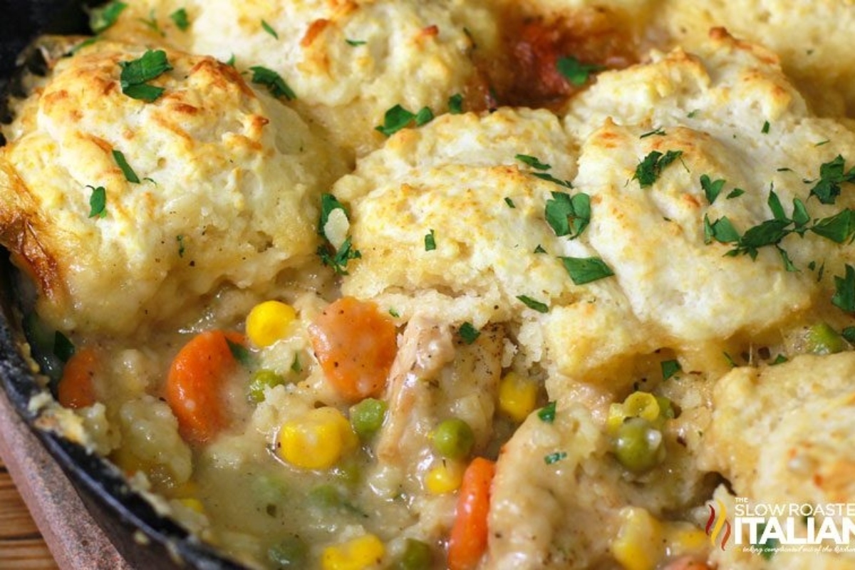 A close-up of a chicken pot pie with a golden biscuit topping and visible vegetables like carrots and peas.