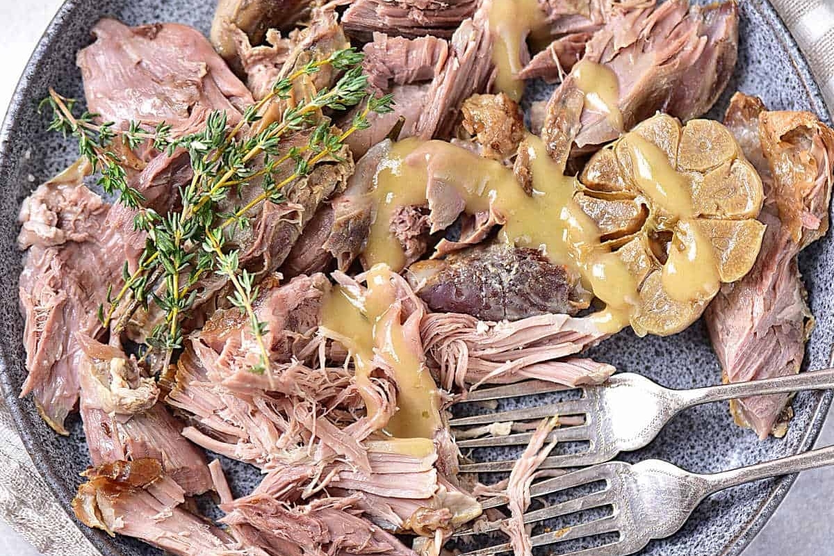 Slow-cooked pulled lamb garnished with fresh thyme and served with a drizzle of gravy.