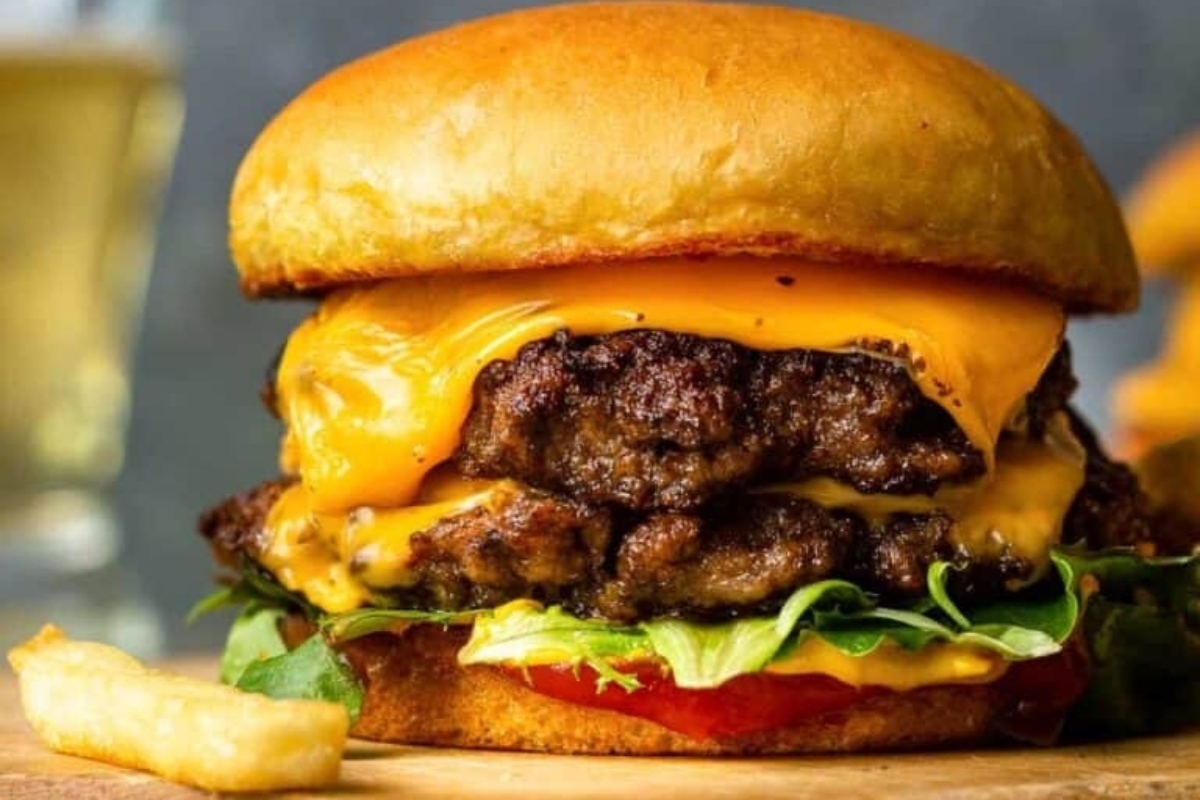 A burger with cheese and fries on a wooden cutting board.