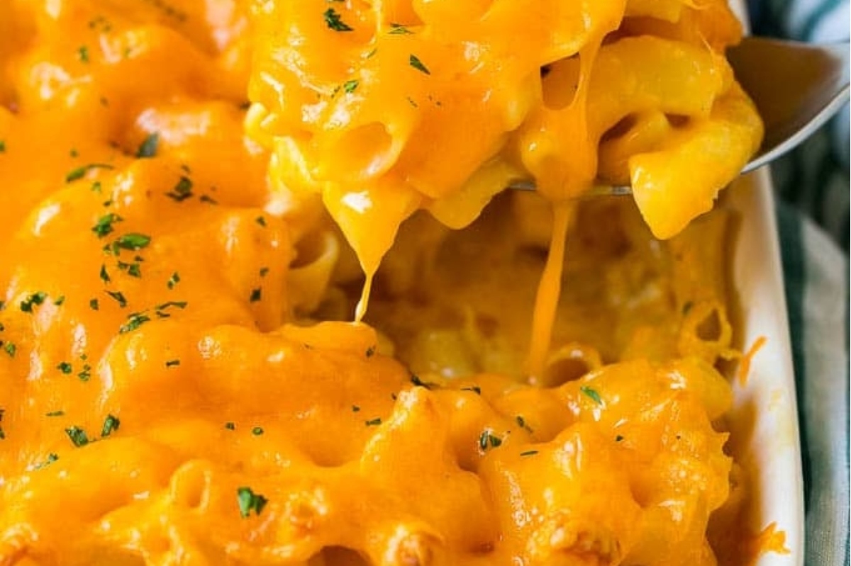 Spoon lifting creamy macaroni and cheese with melted cheese stretching from the dish.
