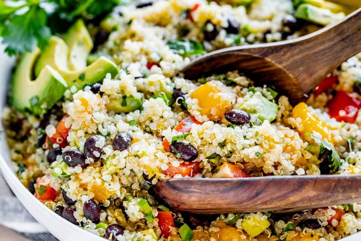 Quinoa salad in a white bowl with wooden spoons.