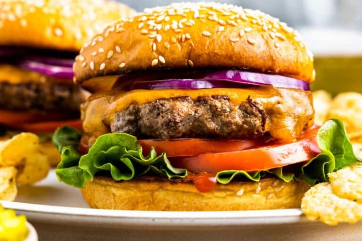 Two burgers on a plate with onion rings and potato chips.