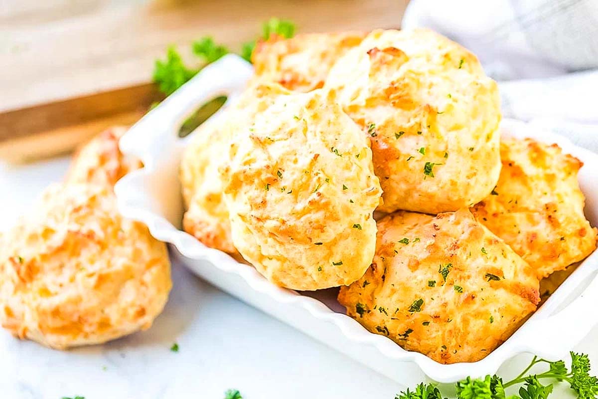 A platter of freshly baked cheddar cheese biscuits garnished with parsley, served on a white dish.