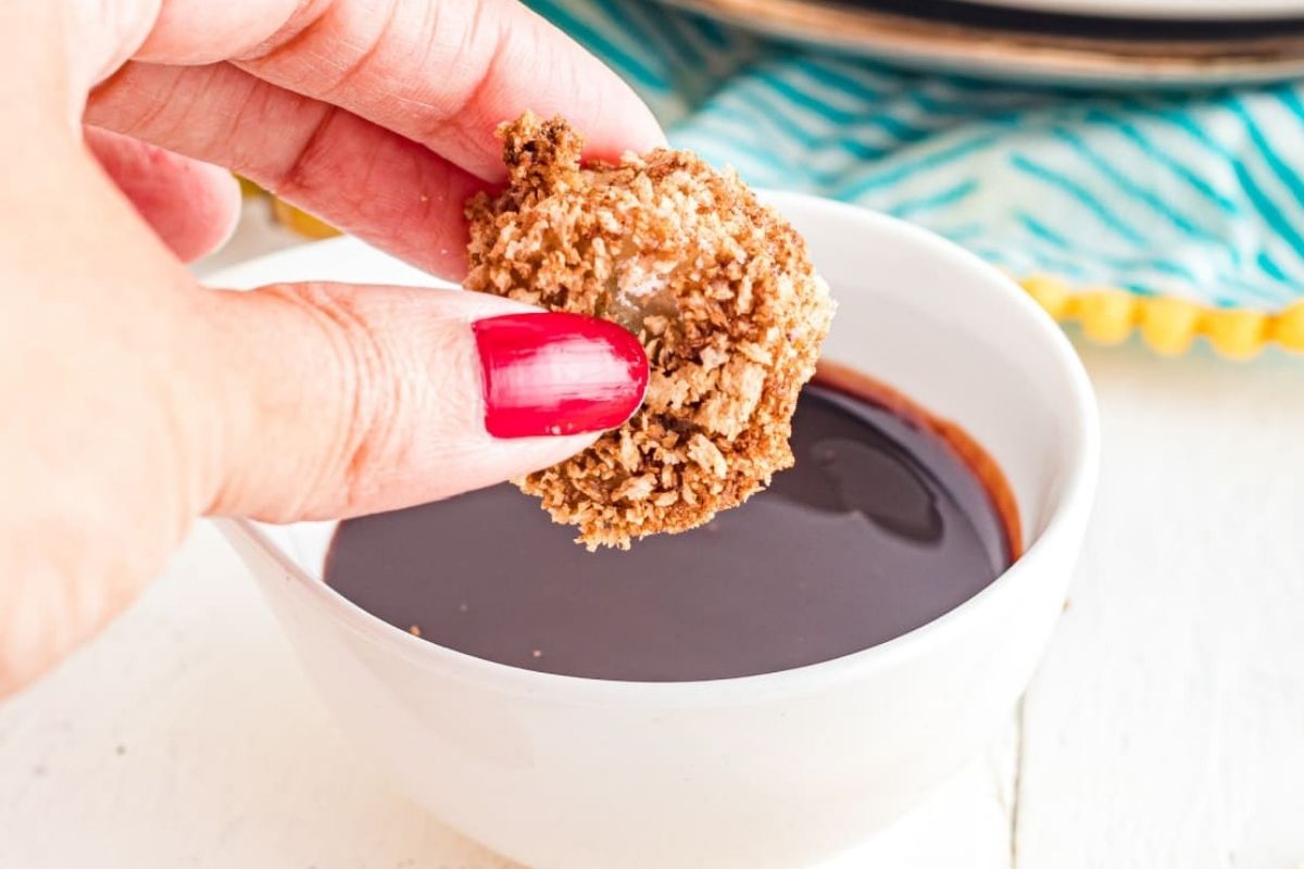 A fritter being dipped in chocolate sauce.