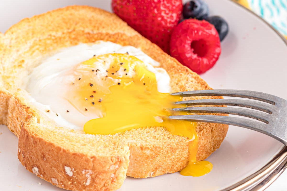 A slice of toast with a sunny-side-up egg and a fork breaking the yolk, accompanied by strawberries, raspberries, and blueberries on the side—a simple yet delightful addition to your favorite egg recipes.