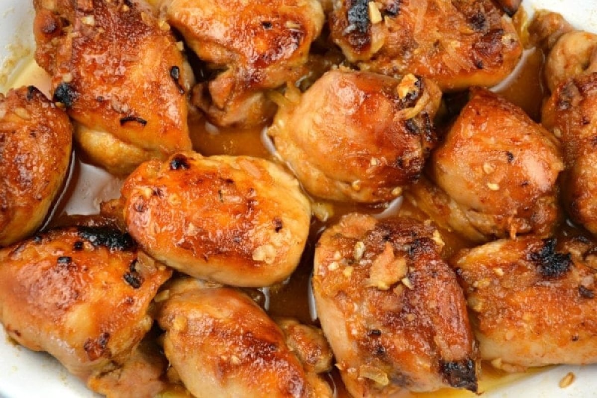 Close-up of a dish with baked chicken thighs glazed in a brown sauce, showing a golden, crispy texture with bits of seasoning and garlic.