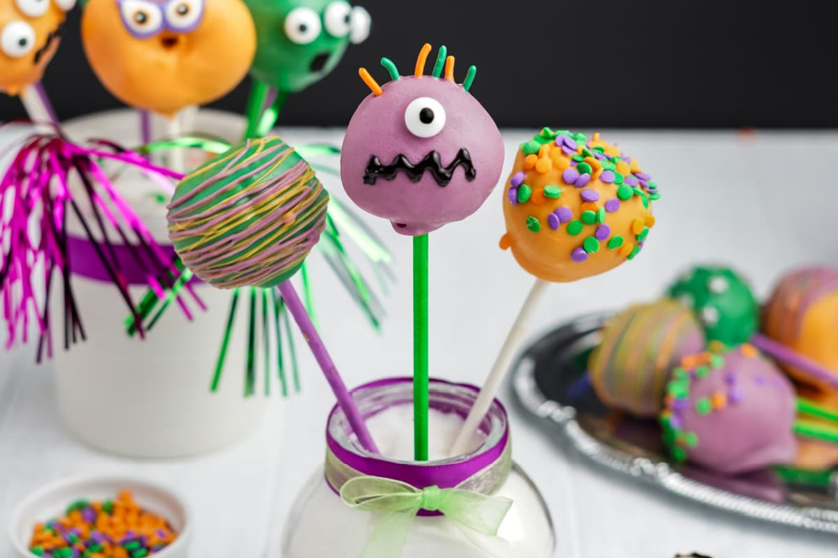 Colorful cake pops decorated with various patterns and sprinkles, featuring one with a monster face and candy eye in the center.