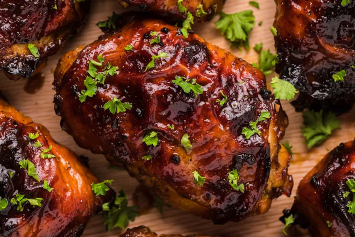 Close-up of several pieces of glazed, grilled chicken garnished with fresh chopped parsley on a wooden surface.