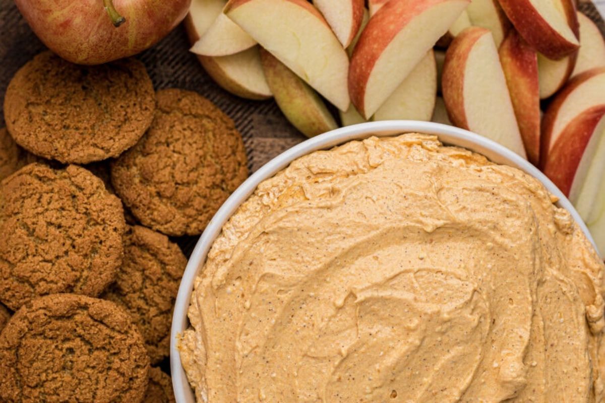 A plate with a pumpkin dip, apples, and cookies.