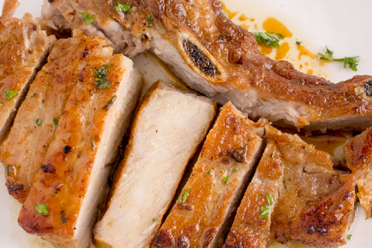 Cooked, sliced pork rib chops garnished with small green herbs and seasoned with spices, displayed on a white plate. This irresistible dish is sure to become a favorite in your collection of repeat pork recipes.