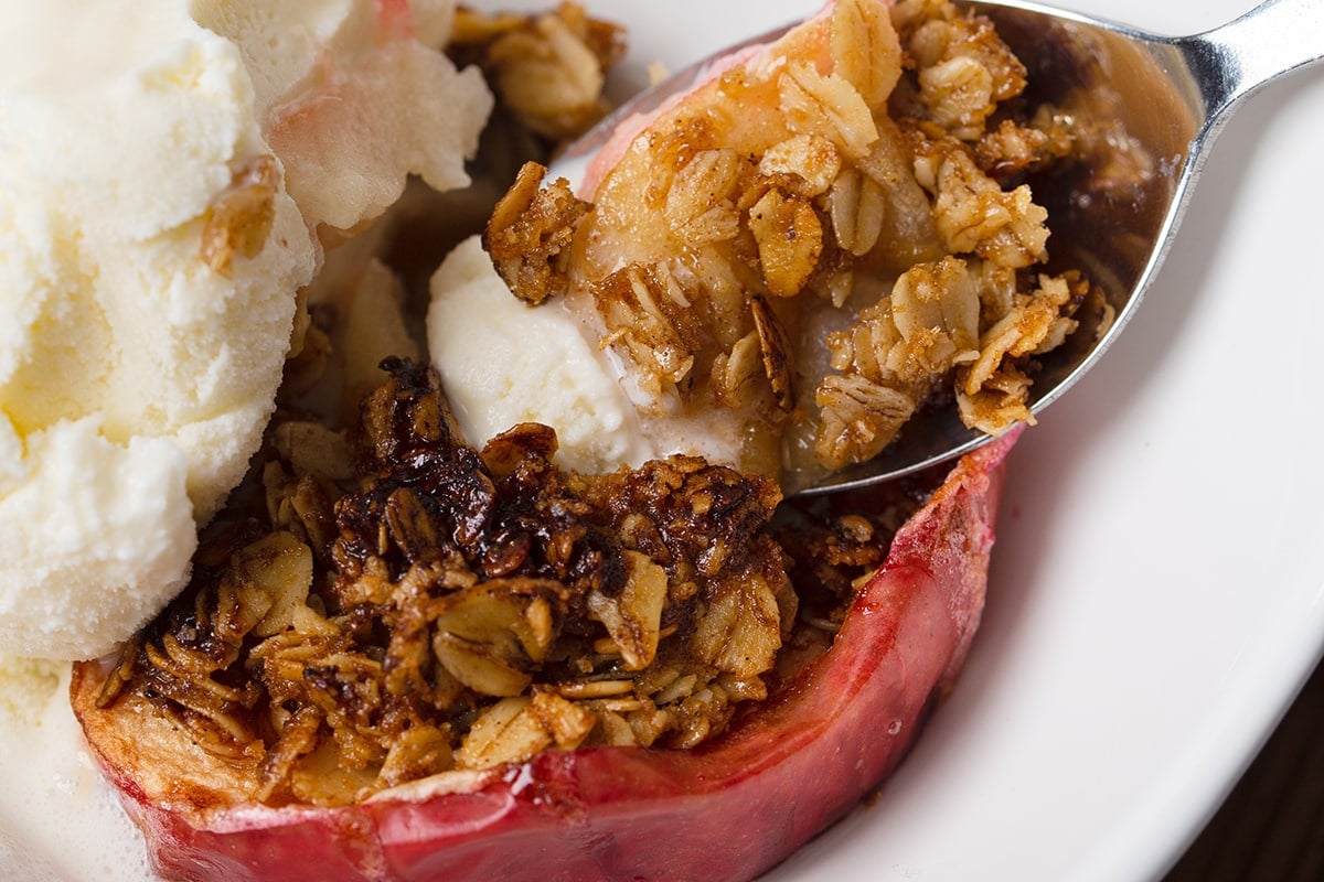 A spoon full of baked apple with some ice cream on top.