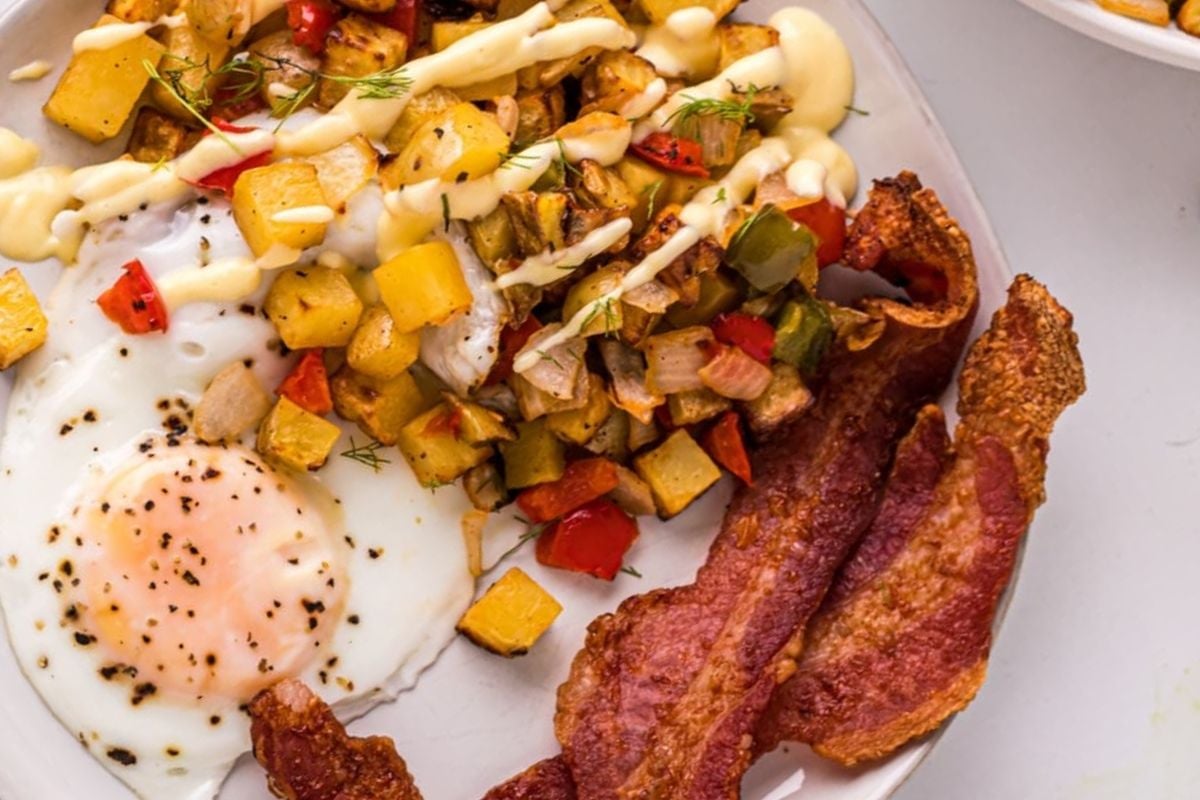 Breakfast potatoes on a plate with eggs and bacon.